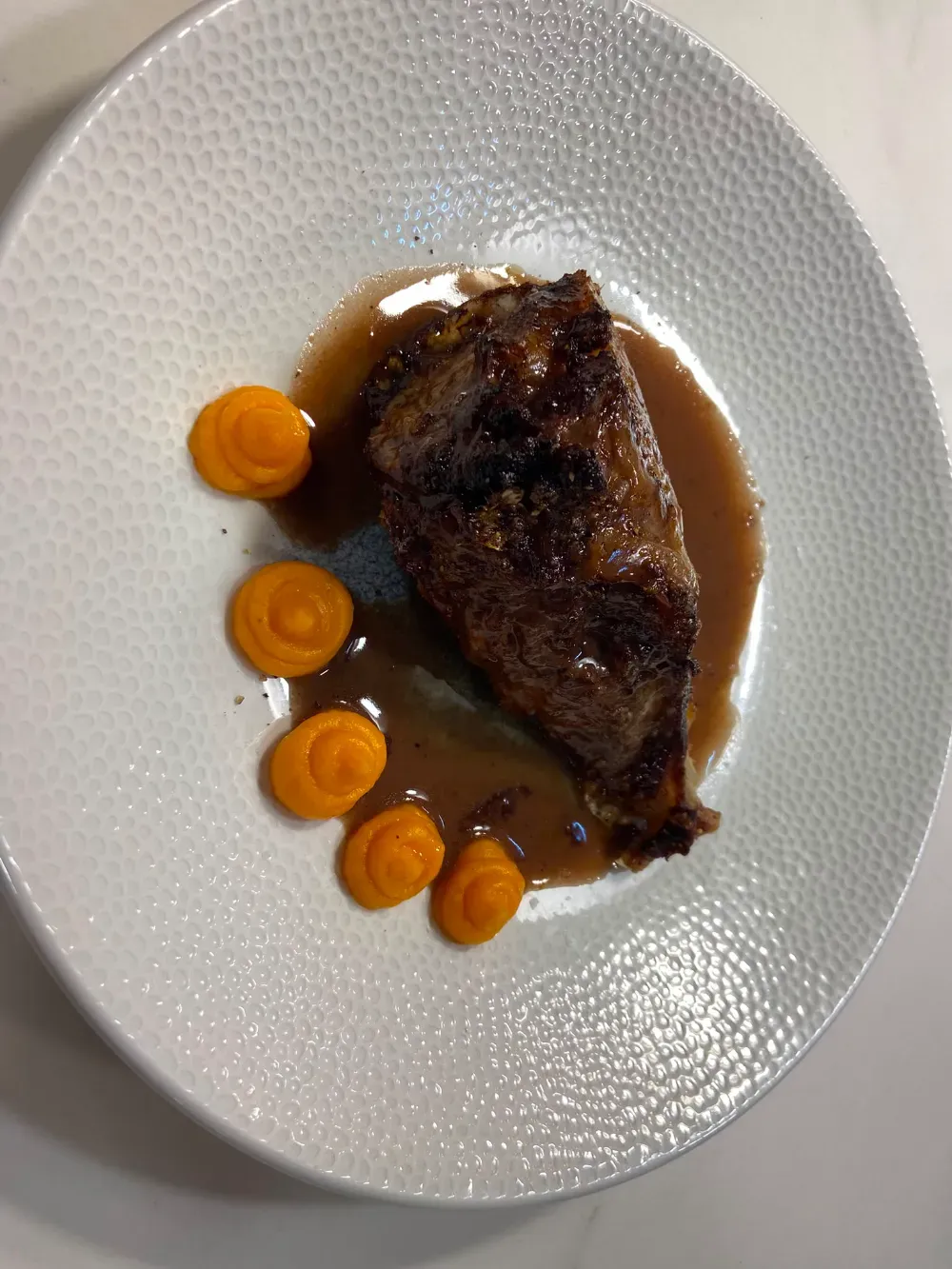 Carne sellada a la plancha con salsa marrón y rodajas de verduras naranjas en un plato blanco