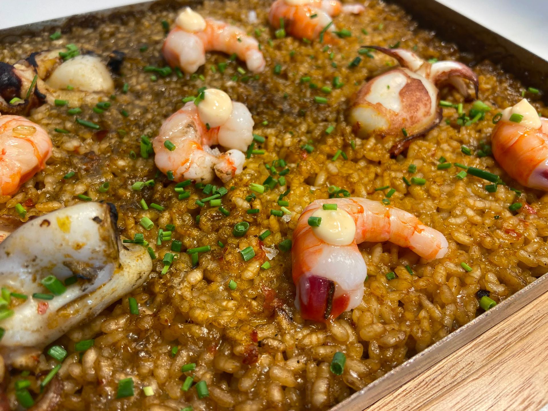 Paella de marisco y gambas en una sartén de madera, con hierbas verdes y gajos de limón por encima