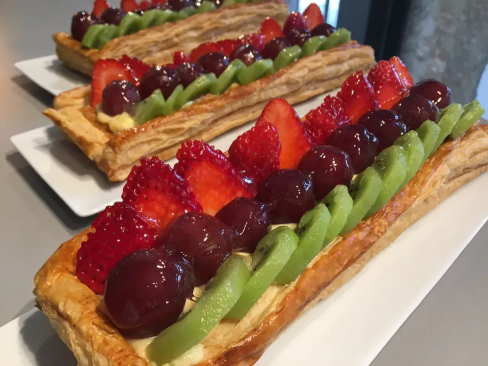 Pasteles con frutas por encima, con fresas, uvas y kiwi, en bandejas blancas