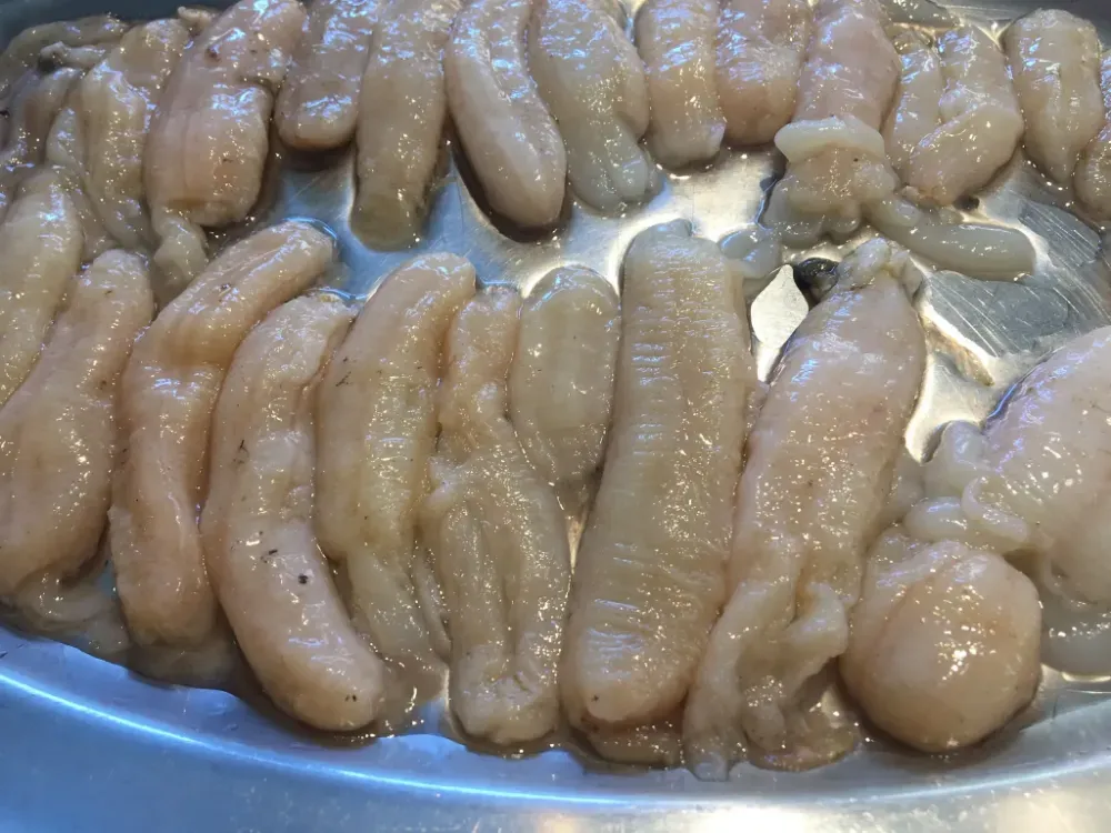 Bandeja con trozos crudos de pescado o carne de color rosa pálido, dispuestos sobre un plato metálico