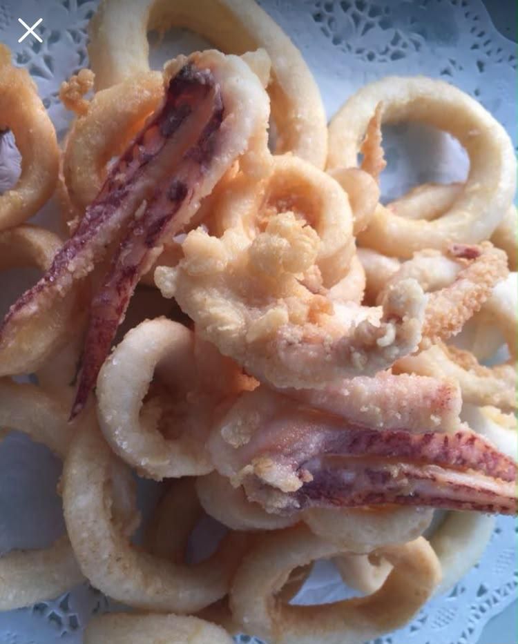 Aros de calamar frito apilados en un plato blanco forrado con una blonda de papel