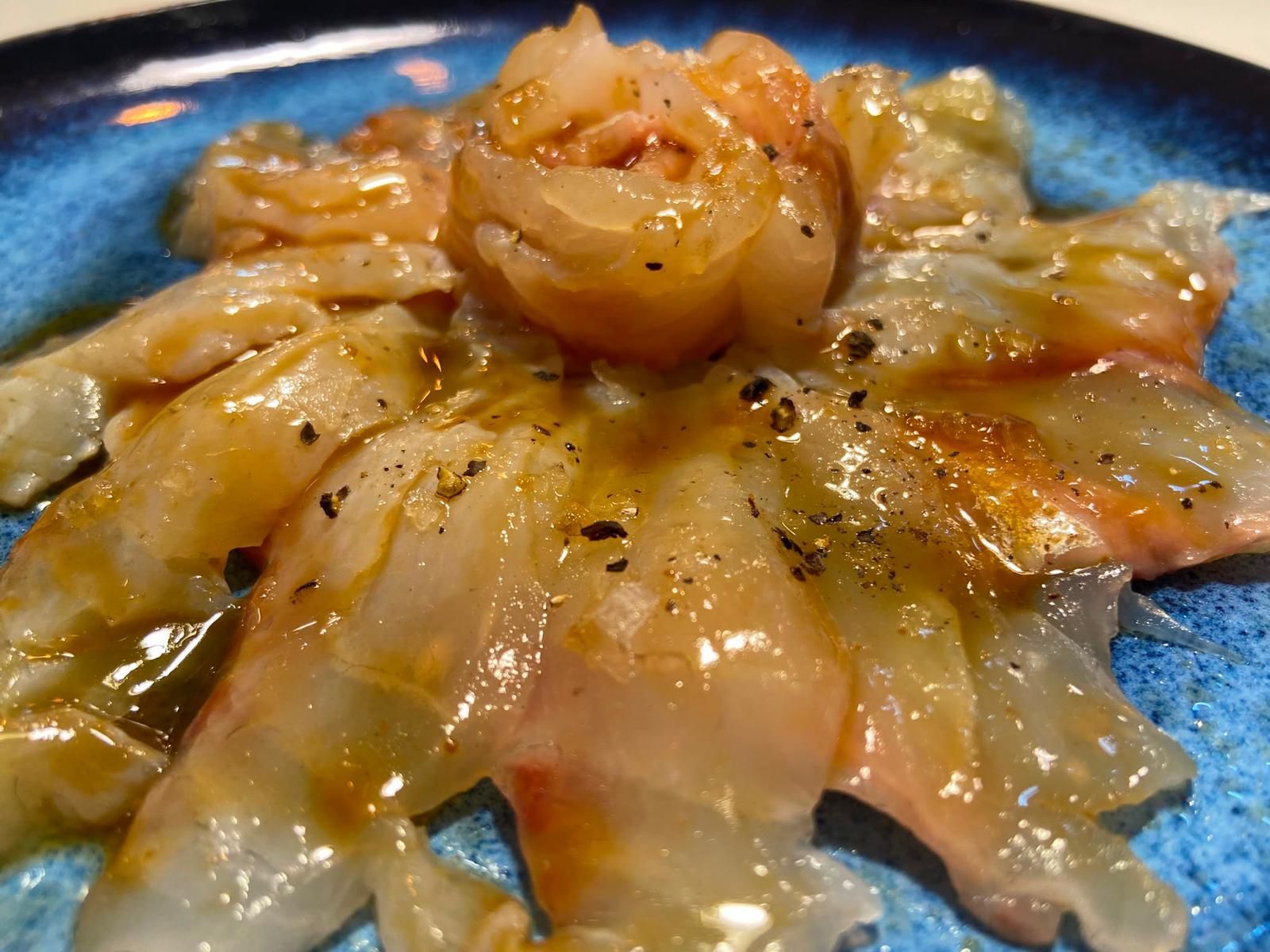 Primer plano de un plato de camarones cocidos con una salsa ligera, servido en un plato azul