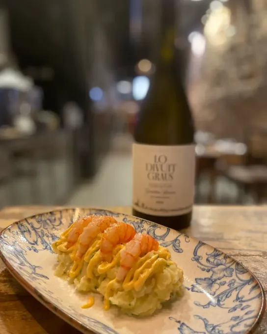 Sushi en un plato estampado con una botella de vino blanco al fondo.