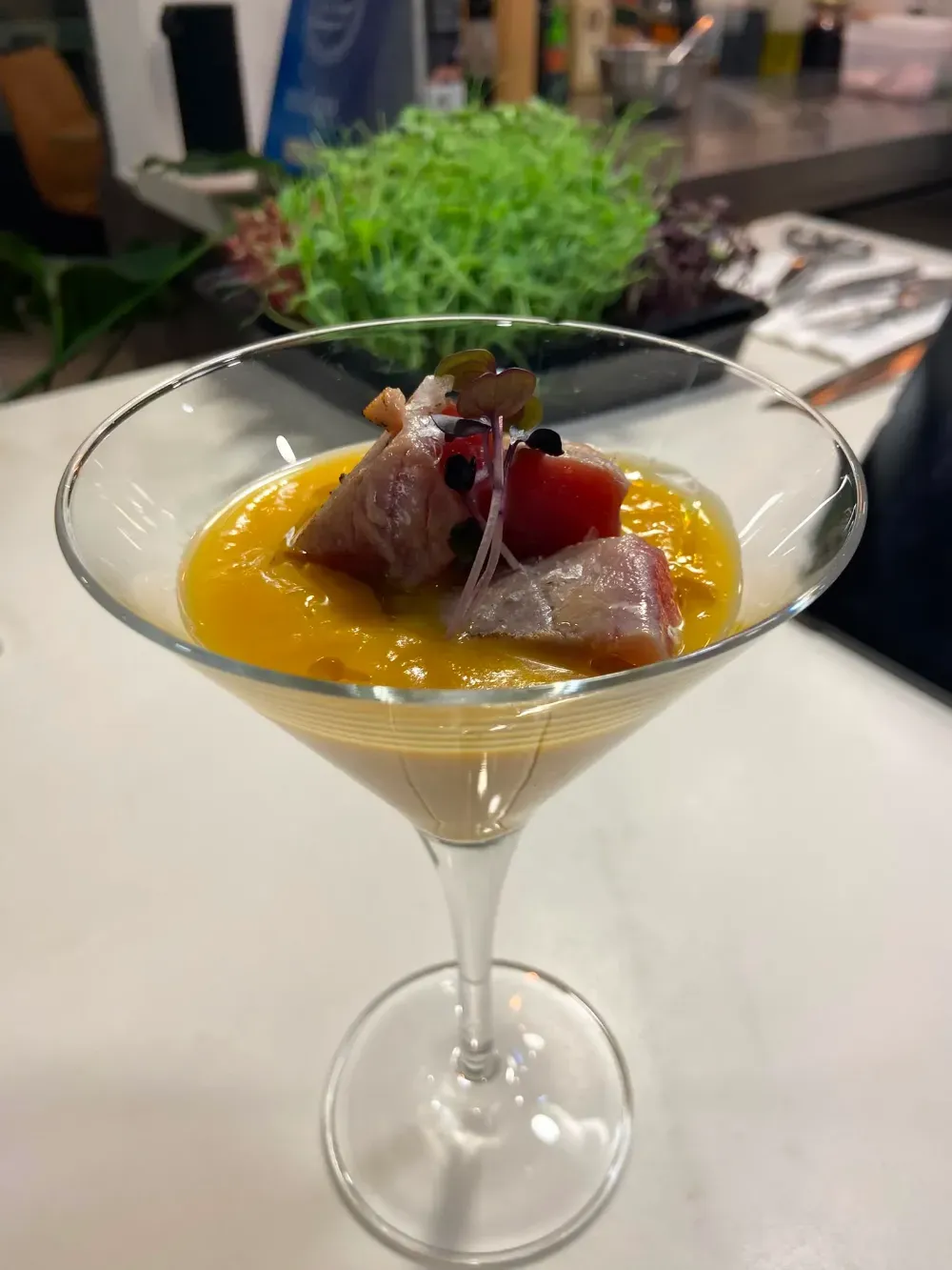 Cóctel de postre con puré de naranja y frutos rojos en una copa de martini, servido sobre una mesa.