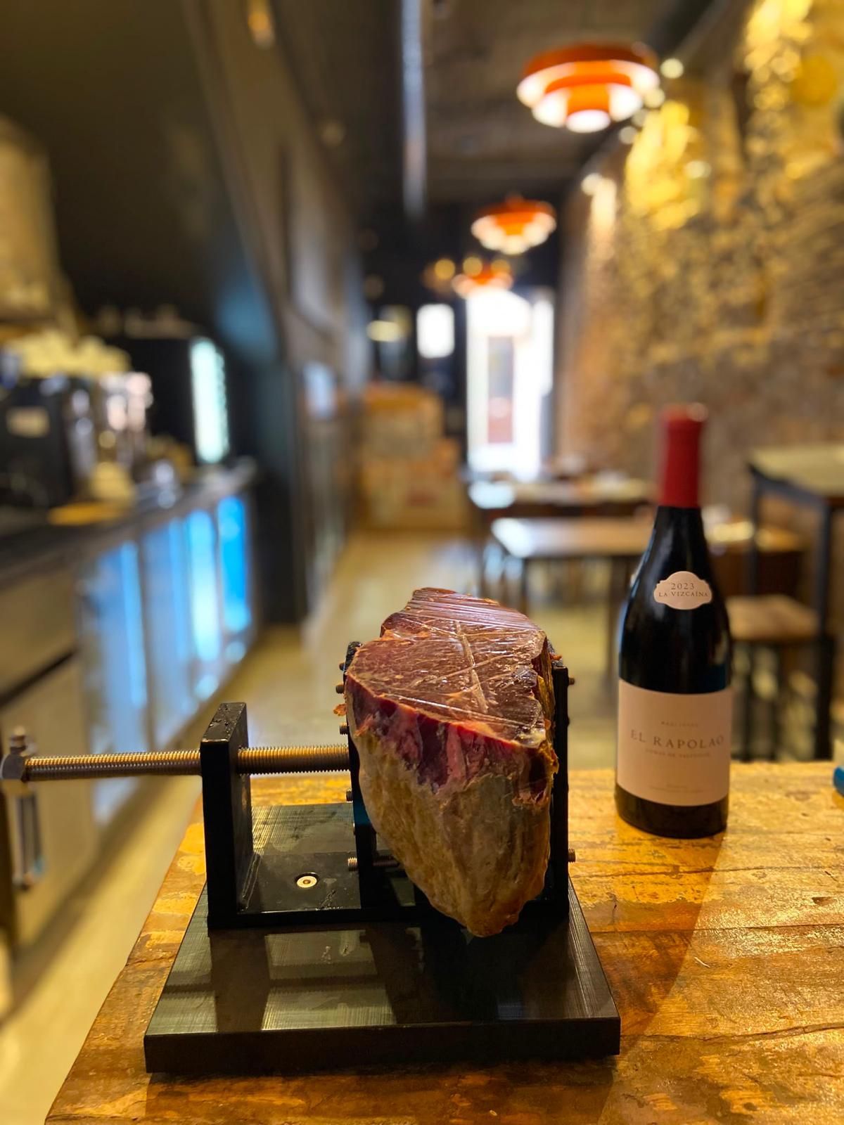 Filete sobre un soporte negro junto a una botella de vino tinto en un restaurante con una iluminación cálida.