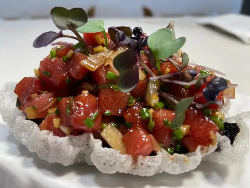Tartar de atún en dados sobre una base crujiente de arroz, coronado con microvegetales y semillas de sésamo