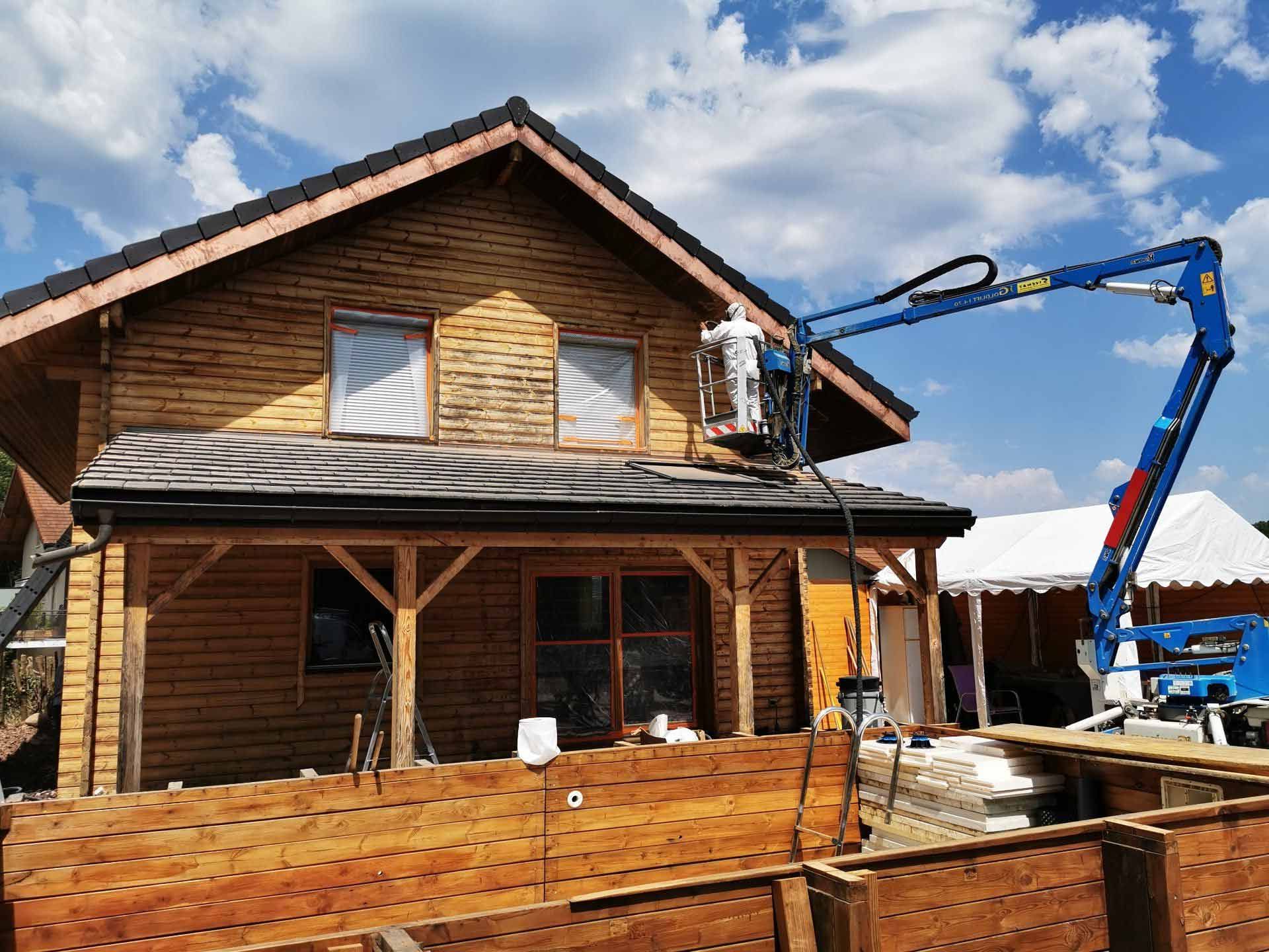 Un expert sur une nacelle pour un traitement de façade d'un chalet en bois