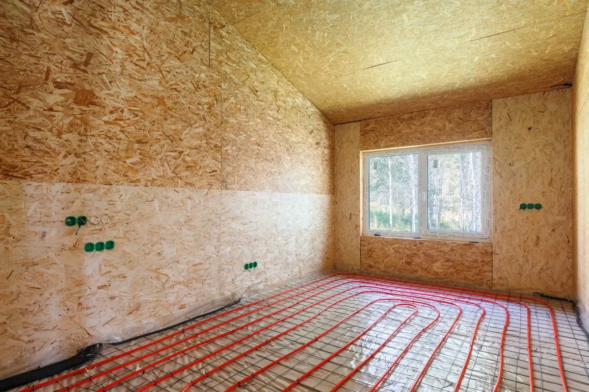 Habitación en construcción con paredes de madera y calefacción por suelo radiante. Ventana al fondo.