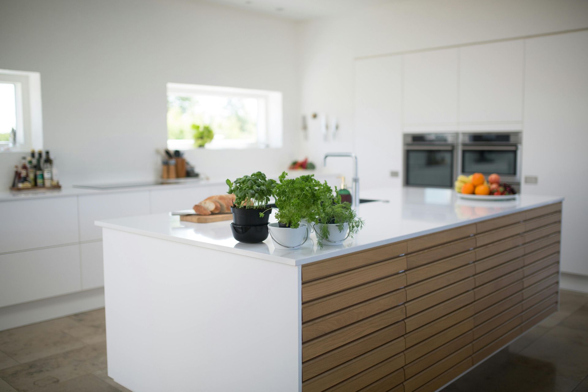 Cocina blanca moderna con isla de madera, con plantas y frutas.