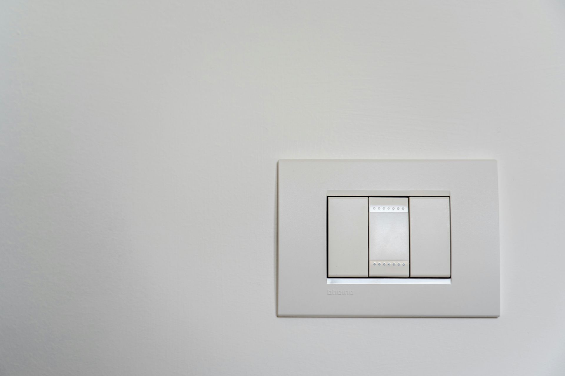 Placa de interruptor de luz blanca sobre una pared blanca con tres interruptores.