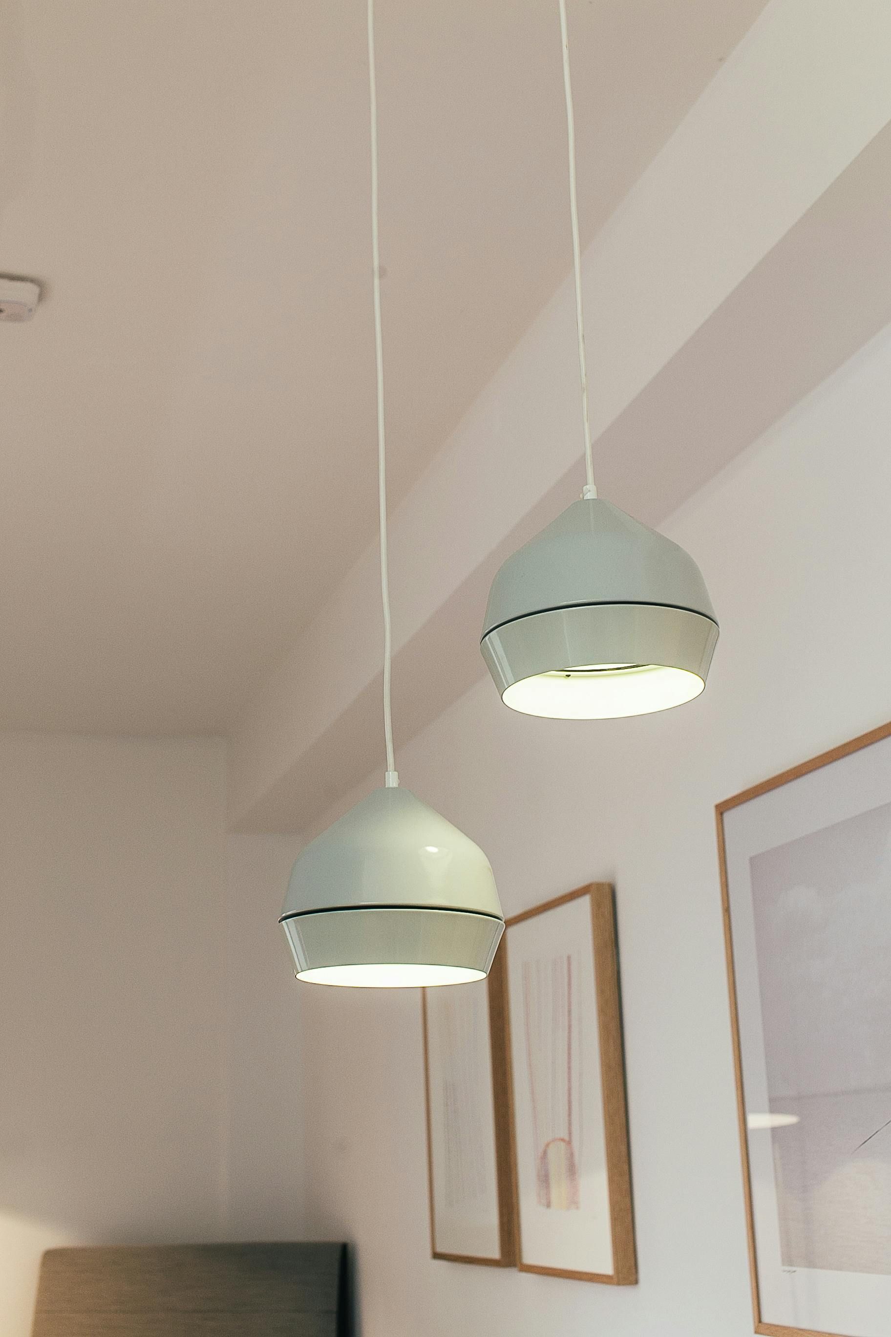 Dos lámparas colgantes de color verde pálido cuelgan de un techo blanco, iluminando una habitación con arte enmarcado.
