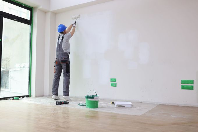 Un hombre está pintando una pared en una habitación vacía.