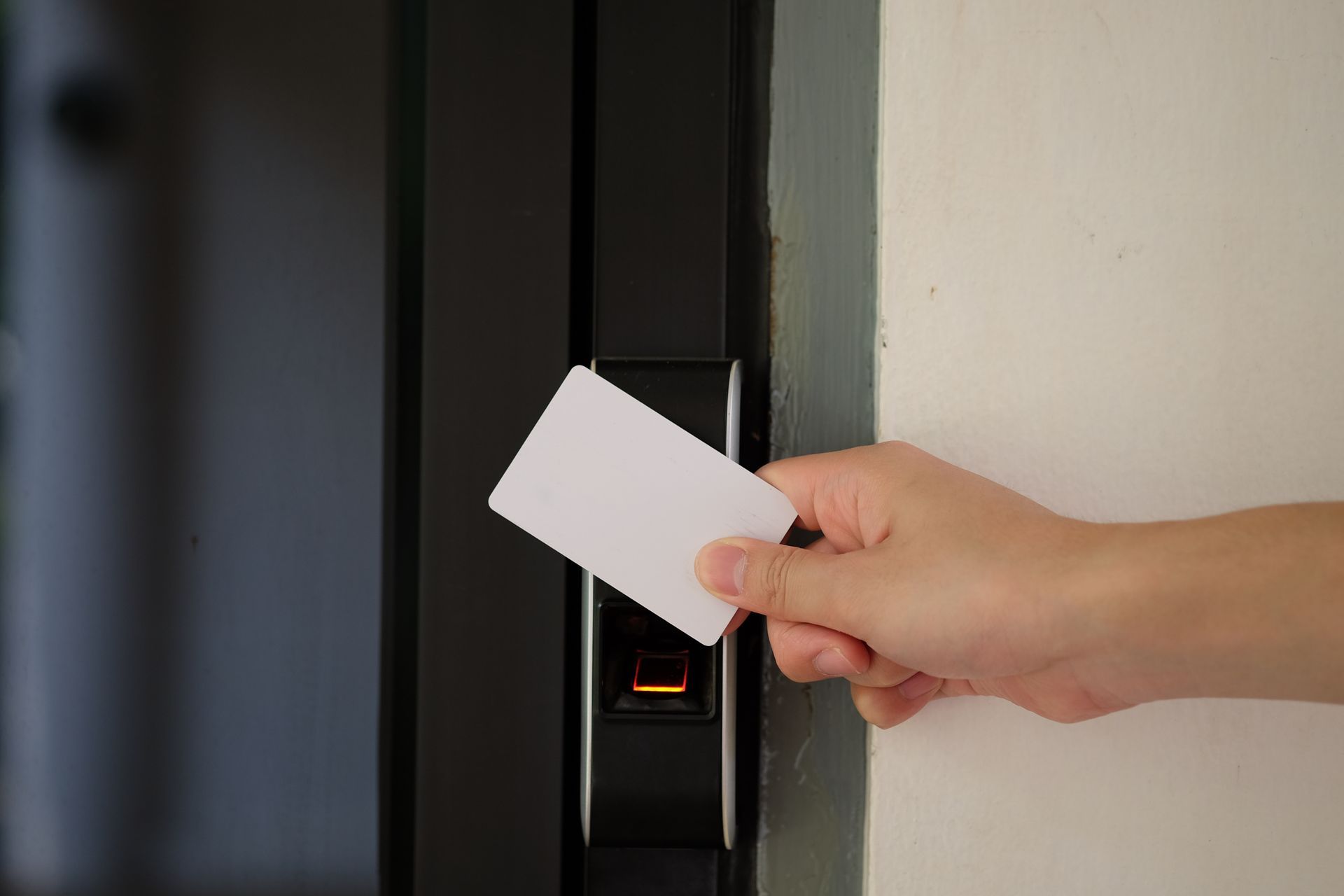 Main tenant une carte blanche au-dessus d'un lecteur de cartes noires sur une porte.