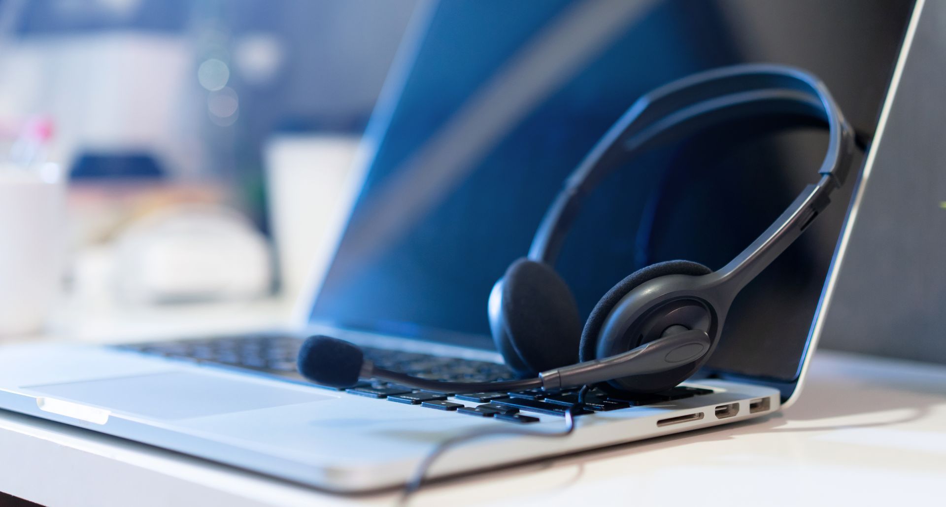 Casque audio sur ordinateur portable, focalisé sur un microphone, fond de bureau blanc.