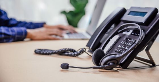 Téléphone fixe avec casque, ordinateur portable en arrière-plan. Une personne utilise l'ordinateur portable.