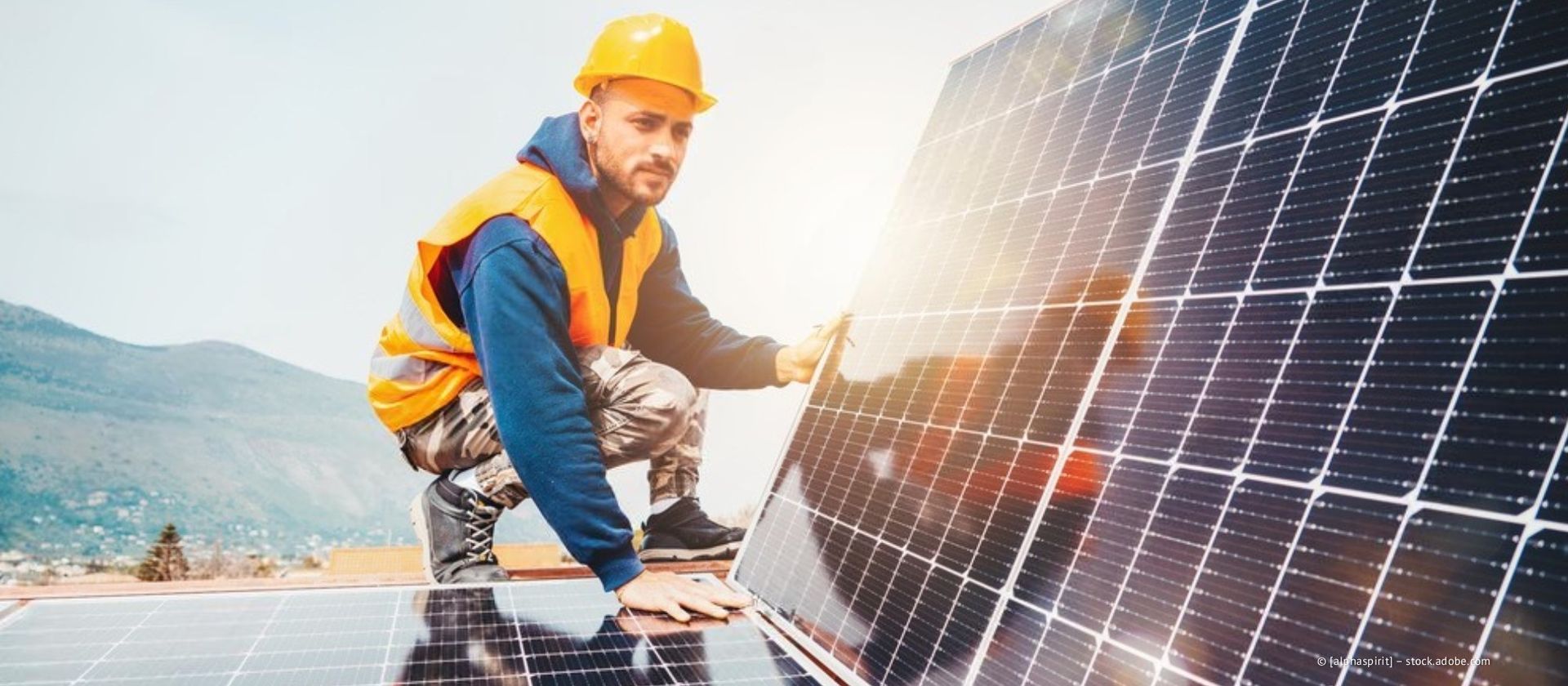 Arbeiter installiert bei Sonnenuntergang Solarpaneele auf einem Dach.