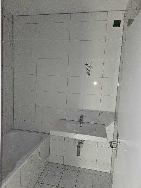 Weiss gefliestes Badezimmer mit Badewanne, Waschbecken und geschlossener Tür.