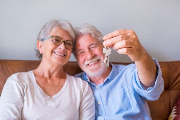 Un couple de personnes âgées est assis sur un canapé et tient les clés.