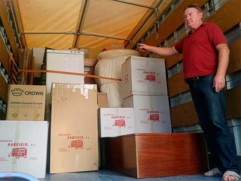 Un hombre con una camisa roja está parado en la parte trasera de un camión de mudanzas.