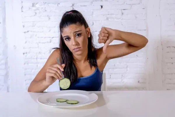 Una mujer está sentada en una mesa con un plato de comida y una rodaja de pepino.