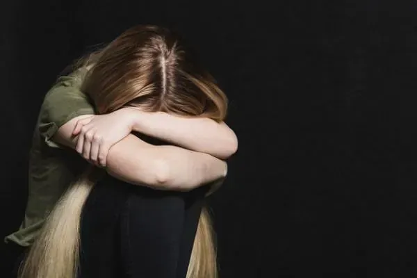 Una mujer está sentada con la cabeza entre las manos.