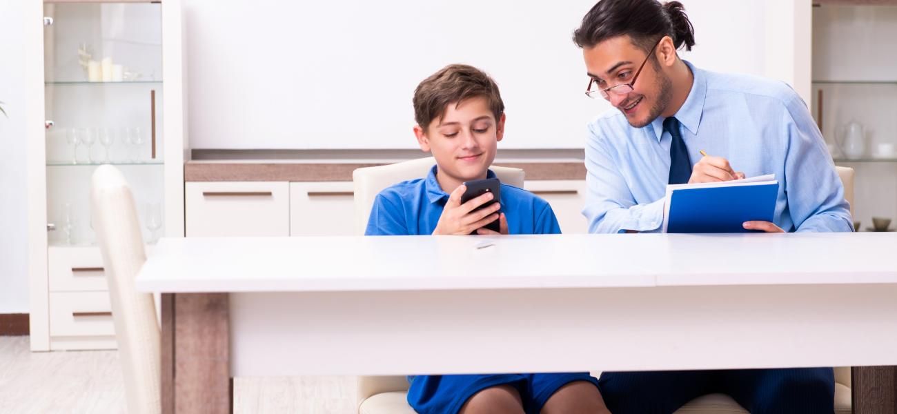 Un hombre y un niño están sentados en una mesa mirando un teléfono celular.