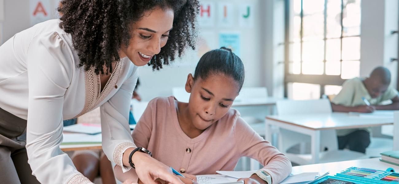 Una maestra está ayudando a una niña con su tarea en un salón de clases.