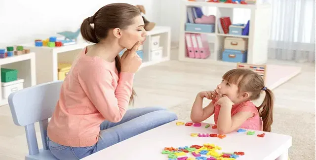 Una mujer está sentada en una mesa hablando con una niña.