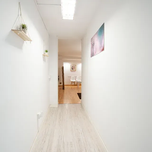 Un largo pasillo con paredes blancas y pisos de madera que conduce a una sala de estar.