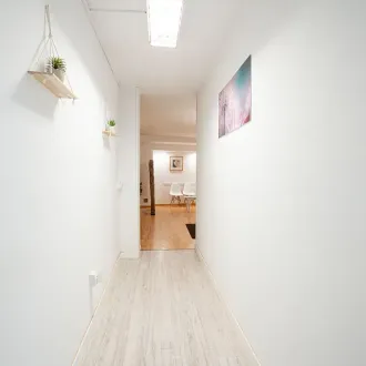 Un largo pasillo con paredes blancas y pisos de madera que conduce a una sala de estar.