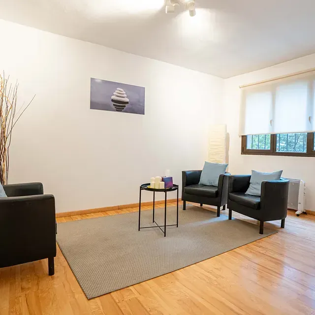 Una sala de estar con dos sillas, una mesa y un barco en la pared.