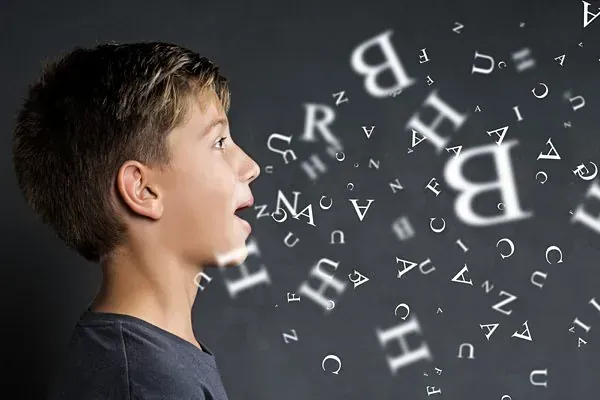 Un niño pequeño está parado frente a una pizarra con letras saliendo de su boca.