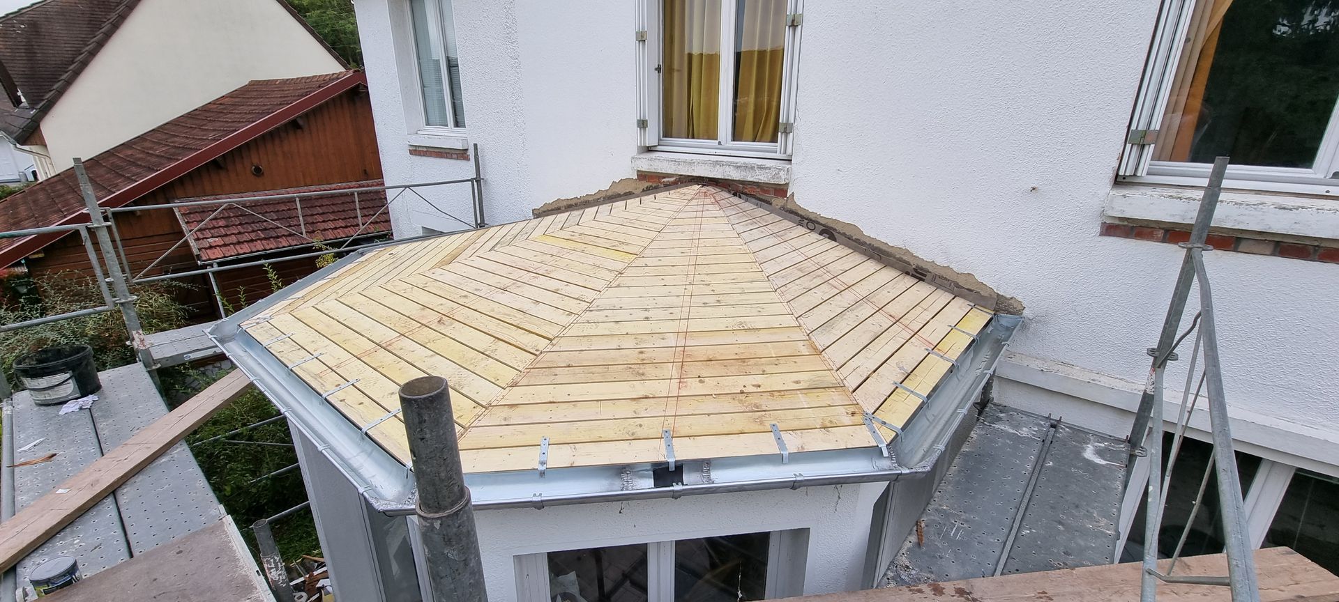 Toiture partiellement construite avec des bardeaux de bois clair et échafaudages à côté d'une maison blanche