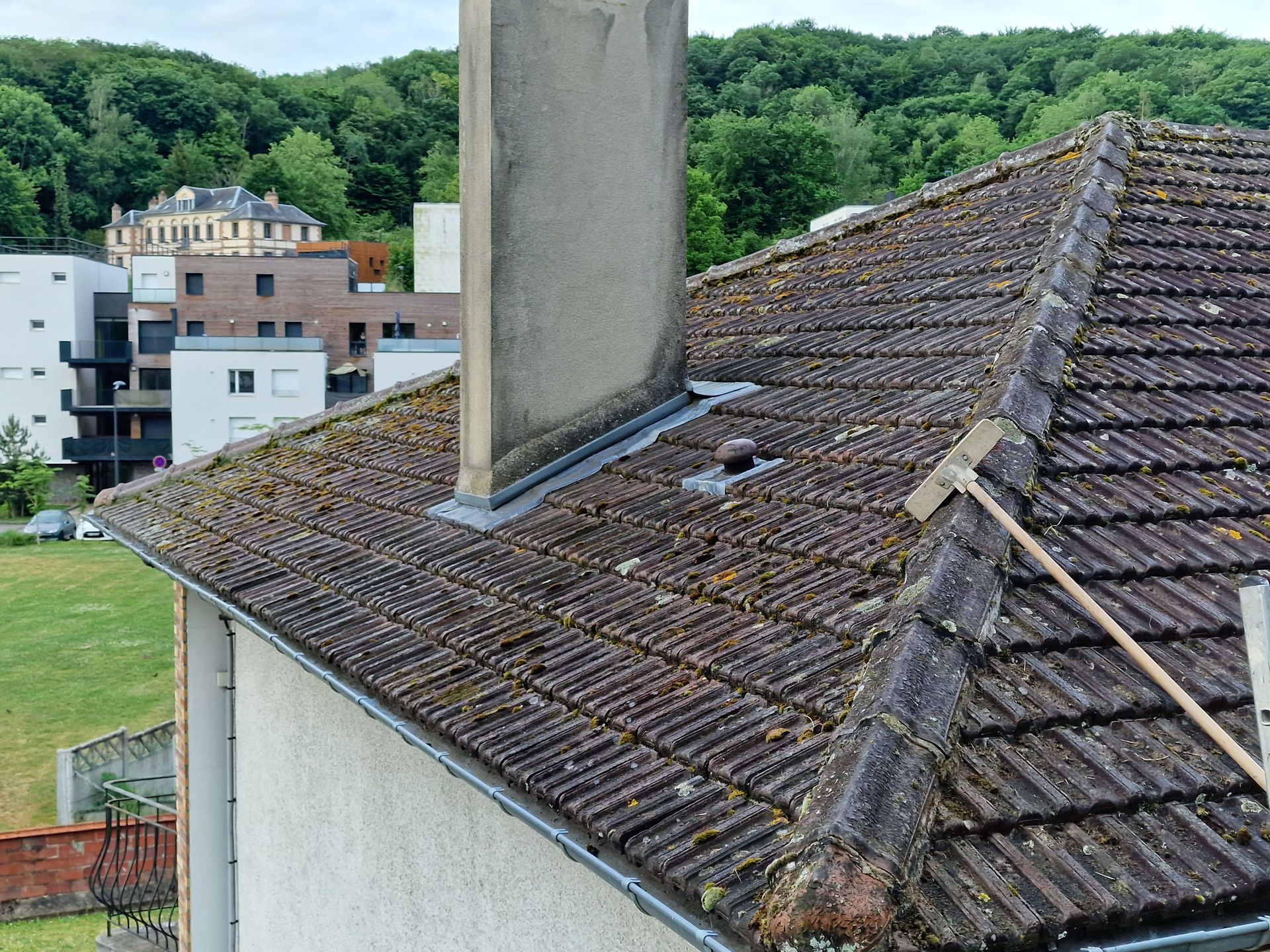 Toit-terrasse avec tuiles patinées et cheminée, donnant sur les collines verdoyantes et les bâtiments environnants