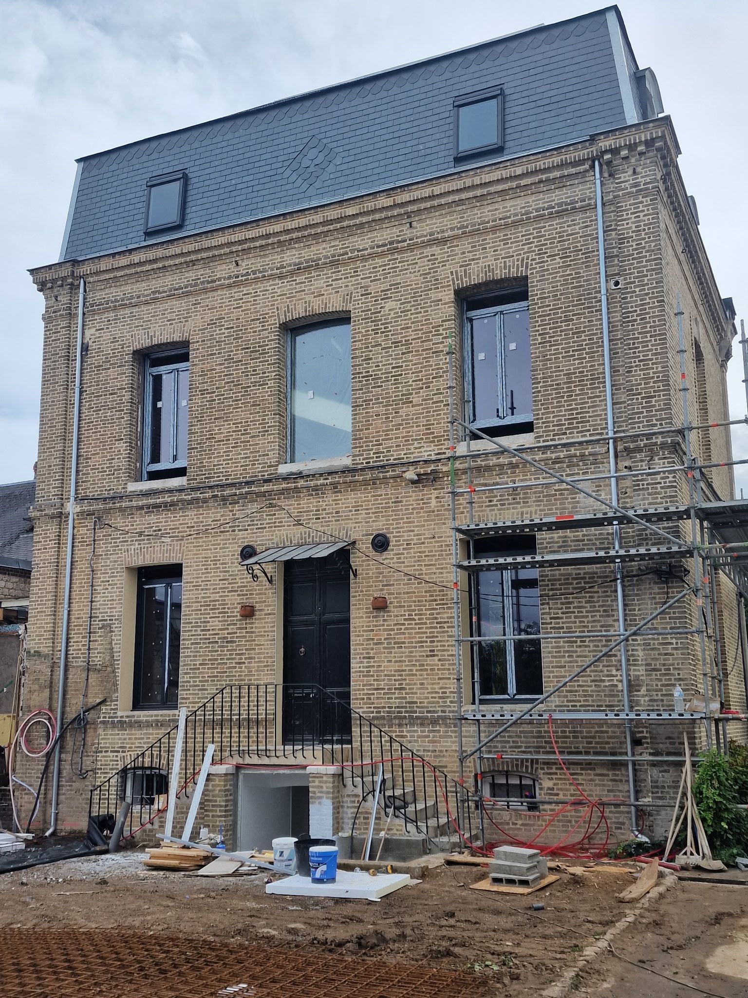 Maison en pierre de trois étages en cours de rénovation, avec des échafaudages et des matériaux de construction apparents à l'avant.