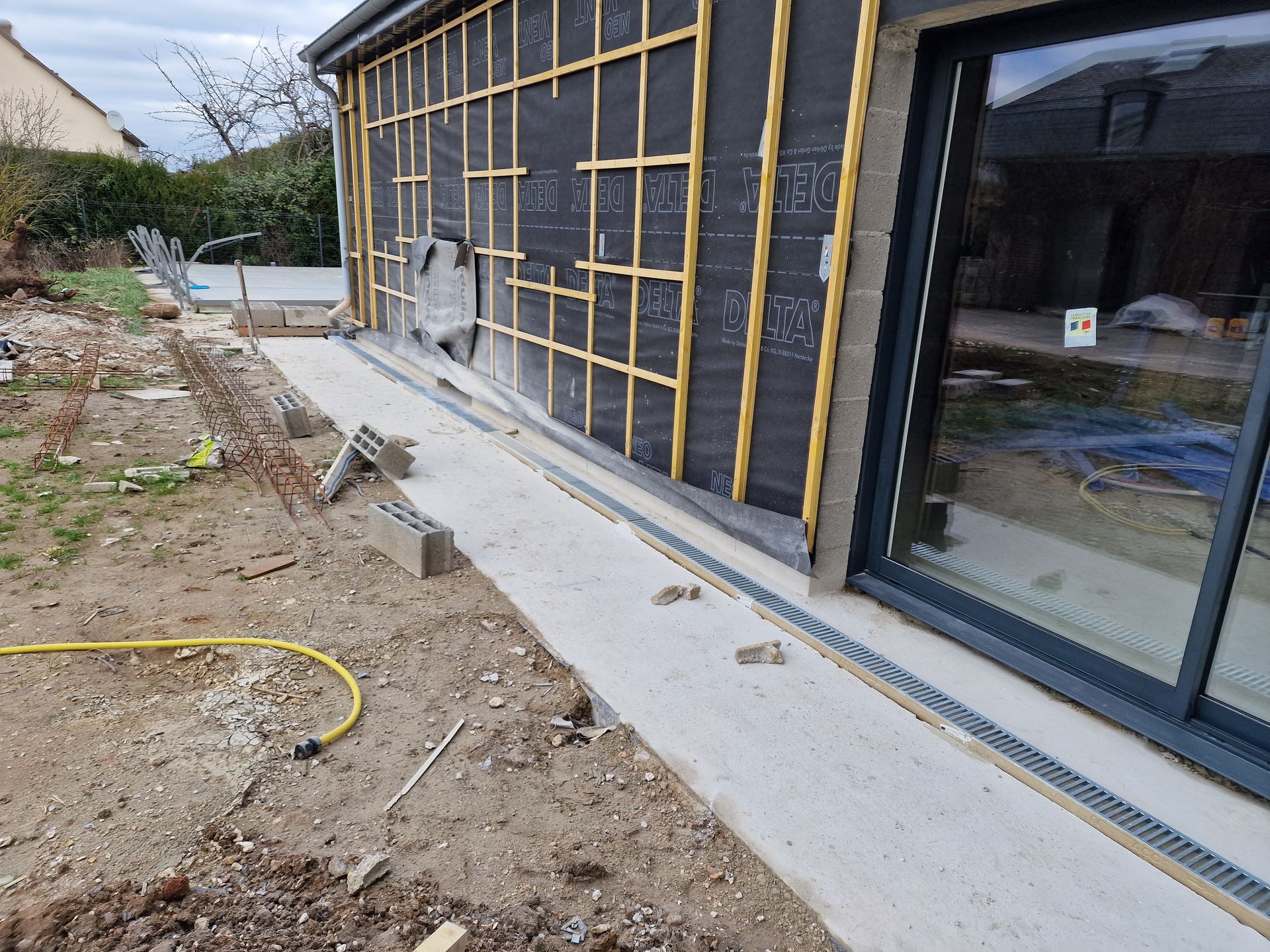 Allée extérieure longeant une maison moderne, avec des matériaux de construction et un aménagement paysager inachevé.