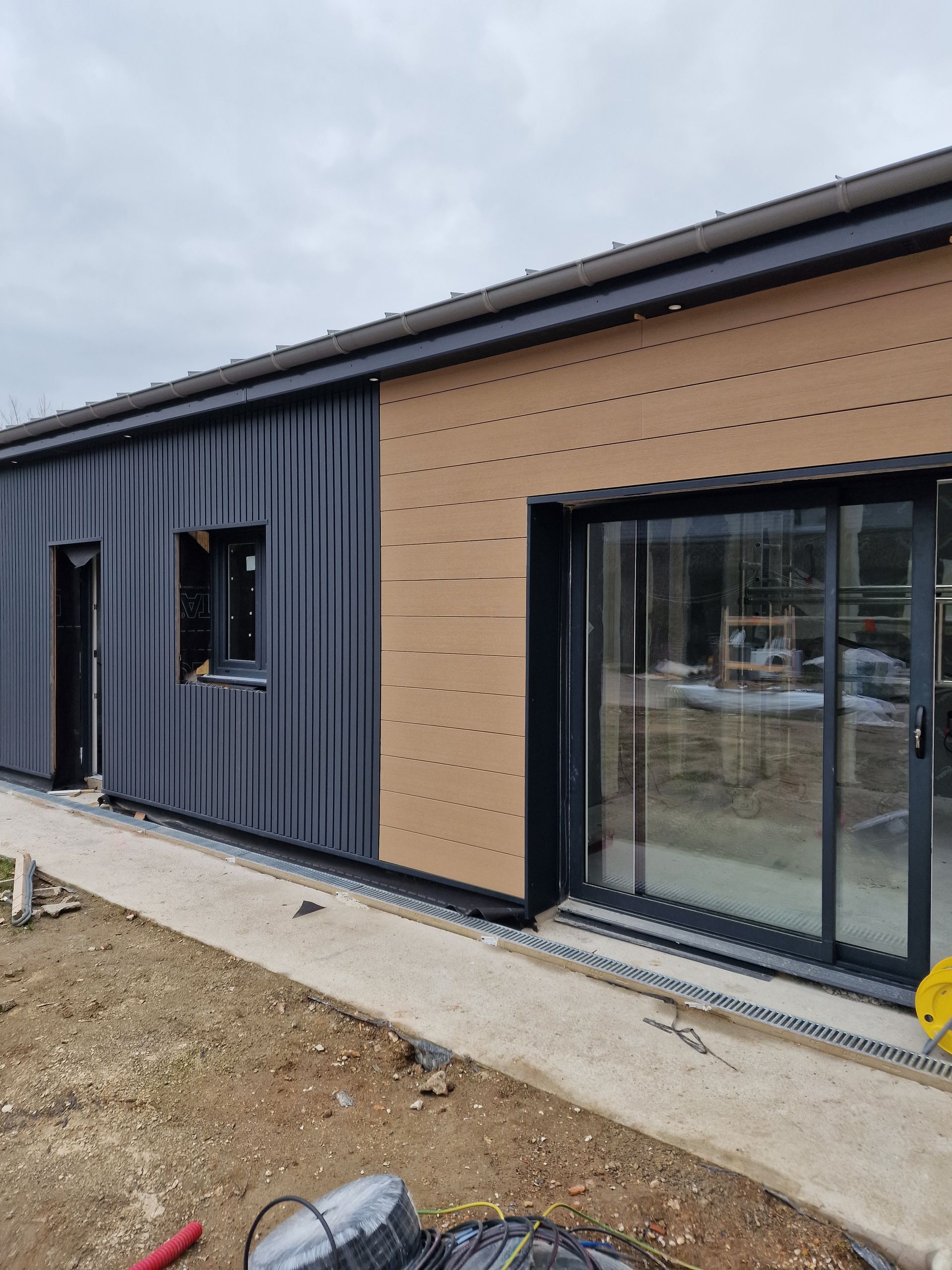 Extérieur d'une maison moderne de plain-pied avec bardage foncé, lambris beige et grandes portes coulissantes en verre