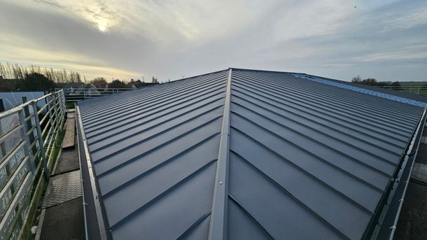 Nouvelle toiture métallique grise en construction, un ouvrier à gauche et un ciel nuageux