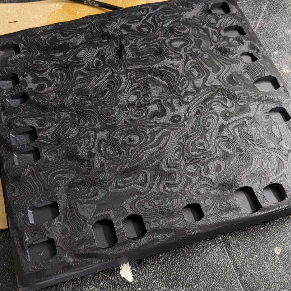 Schwarze Tafel mit einem geschwungenen, marmorierten Muster und ausgeschnittenen Quadraten an den Rändern.