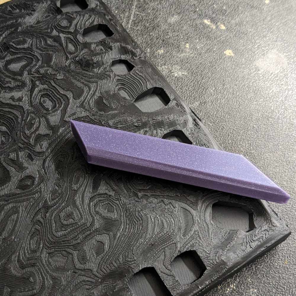 Lila, glitzernder Edelstein auf schwarzem, gemustertem Untergrund mit geometrischen Ausschnitten.