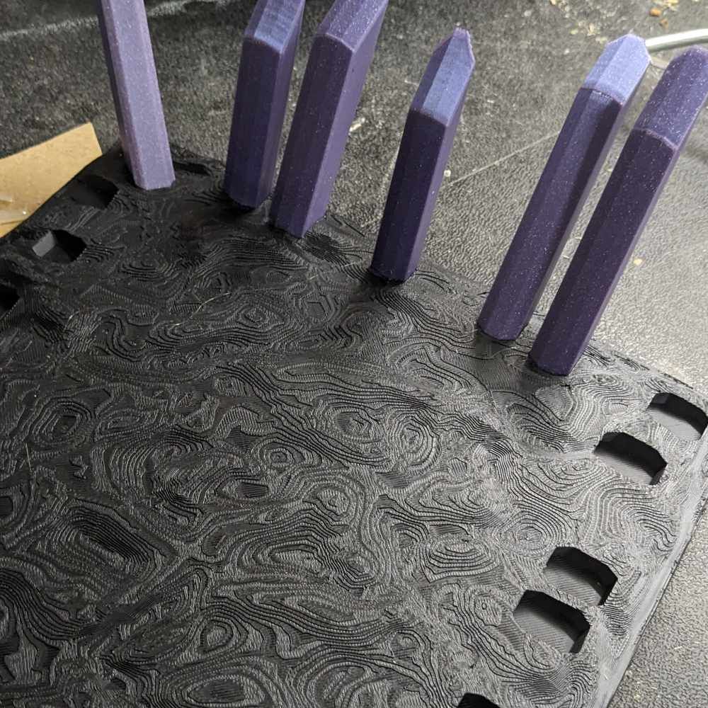 Schwarzer, gemusterter Sockel mit violetten, vertikalen Säulen, die in Schlitze eingesetzt sind.