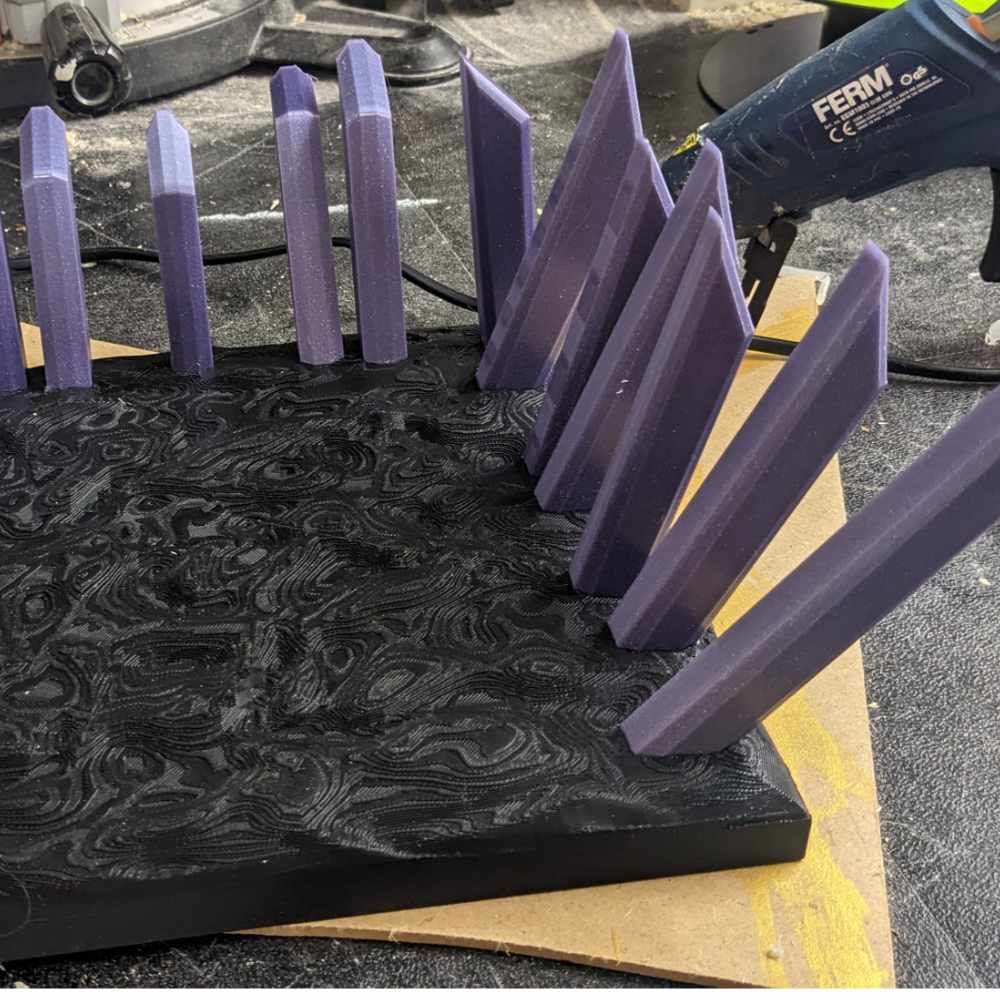 Nahaufnahme von schwarzem, strukturiertem Gelände, auf das violette Kristallformationen geklebt werden, Werkstattumgebung.