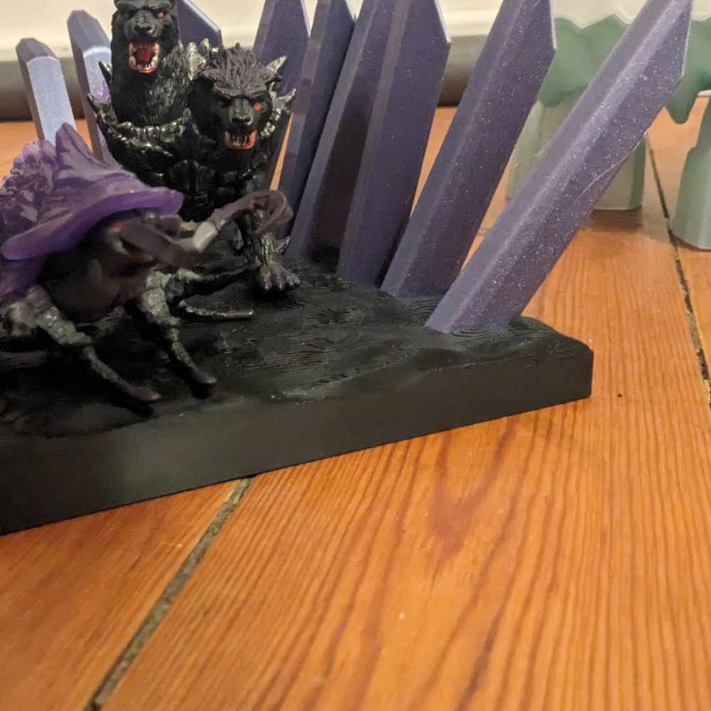 Eine Fantasiefigur mit einem Käfer in einem Hexenhut, Wolfsköpfen und violetten Kristallen auf einer Holzoberfläche.