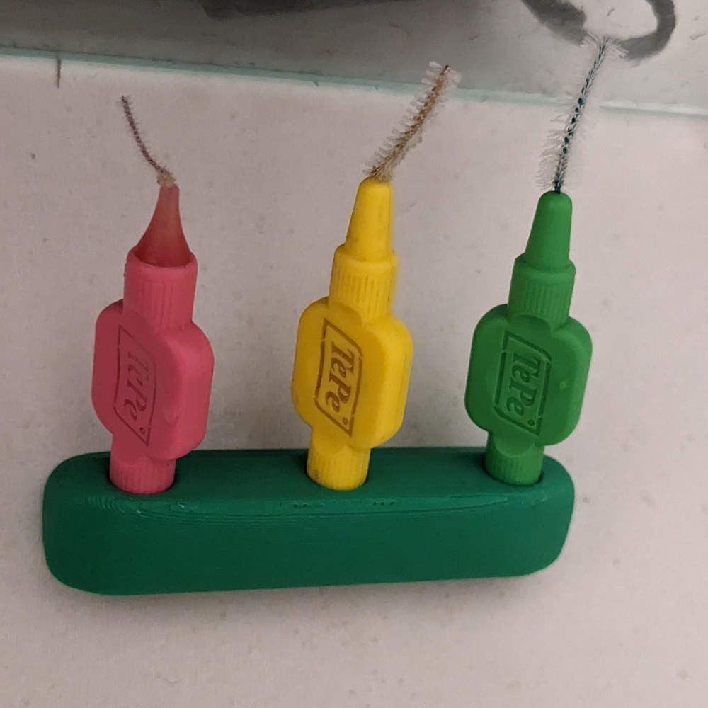 Drei farbige Interdentalbürsten in einem grünen Halter.