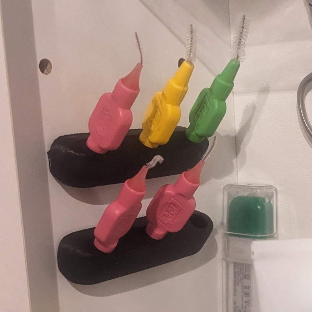 Interdentalbürsten in einem Halter, eine rosa, eine gelbe, eine grüne.