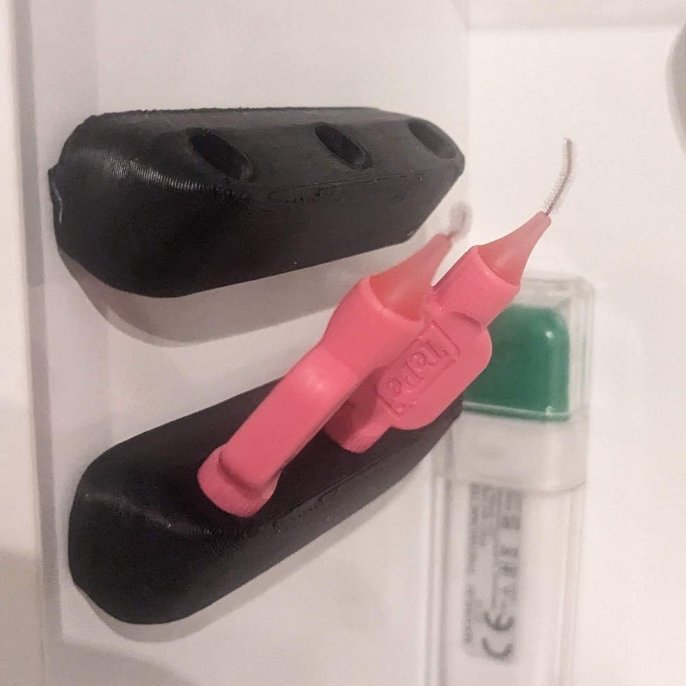 Schwarze, 3D-gedruckte Werkzeuge mit rosa Pinselspitzen; durchsichtige Flasche mit grünem Deckel ist teilweise sichtbar.