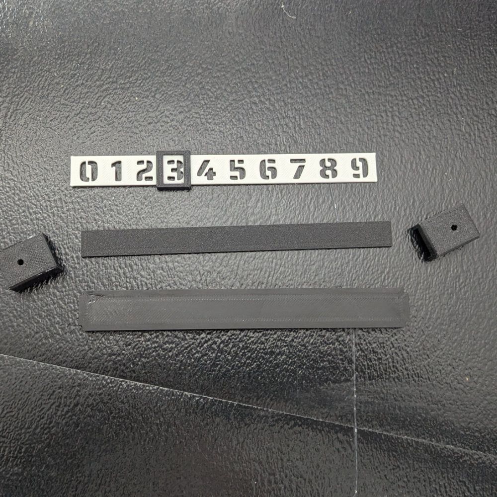 Schwarze Teile: nummerierte Skala, Schaumstoffstreifen, Blöcke. Auf dunklem Untergrund.