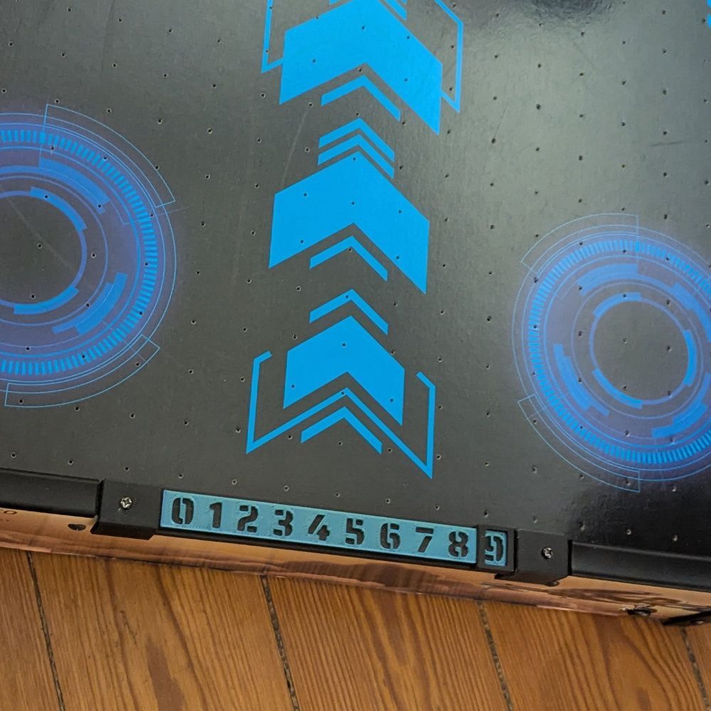 Schwarze Spielfläche mit blauen Pfeilen und kreisförmigen Mustern sowie einer nummerierten Tafel.