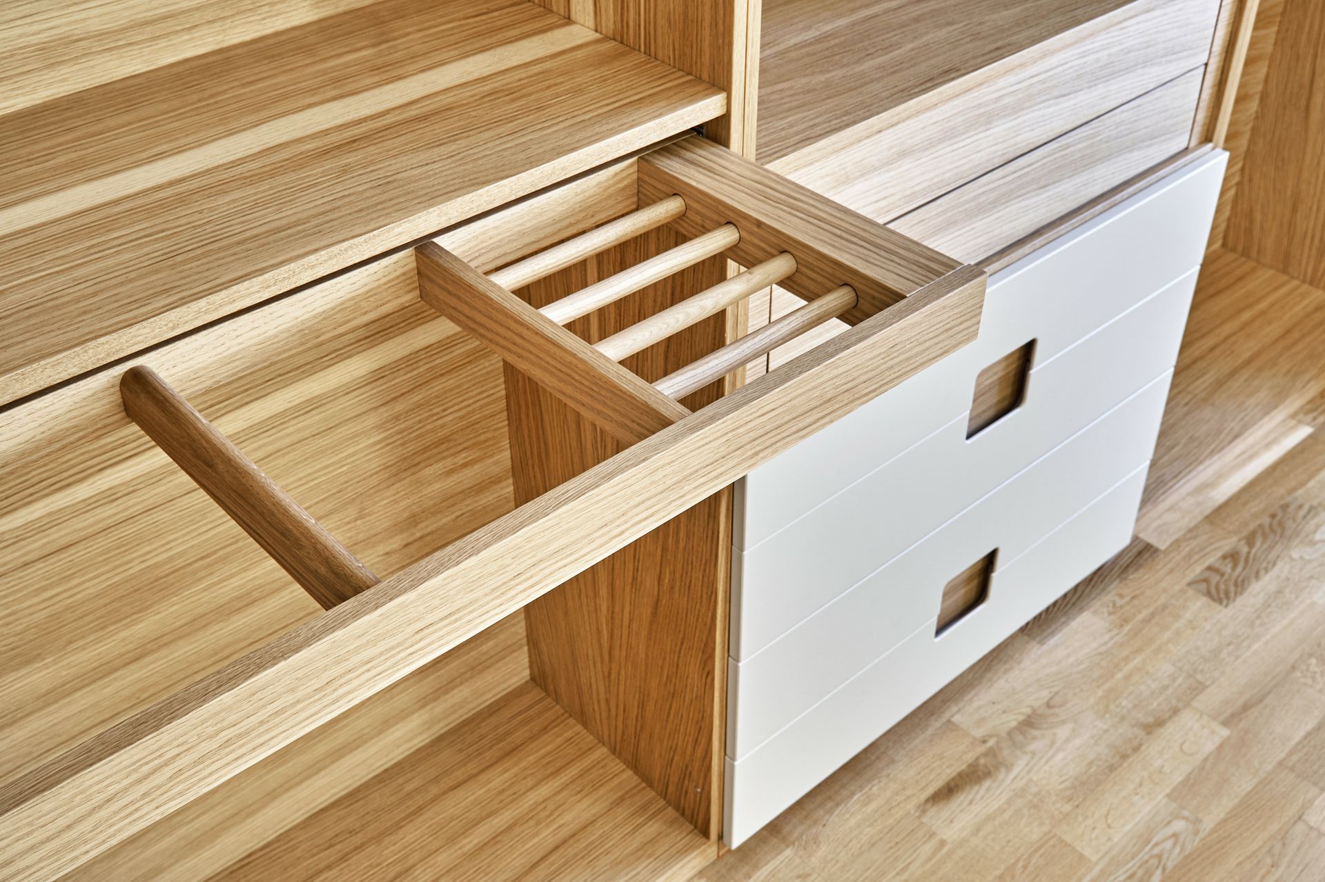 Meuble en bois avec étagère coulissante à tiges, à côté de tiroirs blancs à découpes carrées.