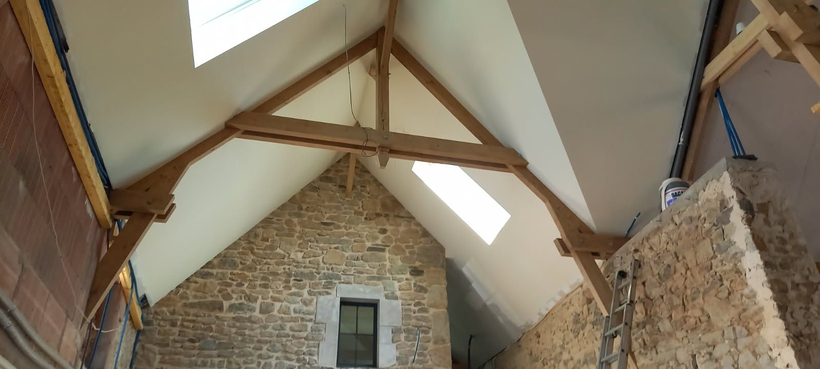 Vue intérieure d'une pièce aux murs en pierre avec poutres en bois et une fenêtre dans le toit.